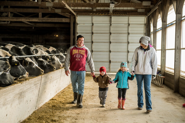 Farm family walking in their barn with cows to the left.