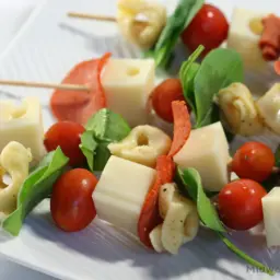 Skewers with pasta, basil, tomatoes, pepperoni, and cubes of cheese.