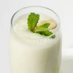 Glass of apple yogurt smoothie garnished with mint and an almond.