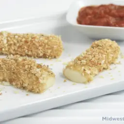 Baked mozzarella sticks on a plate with a side dish of marinara.