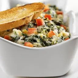 Baked spinach artichoke yogurt dip in atoast-topped dish.