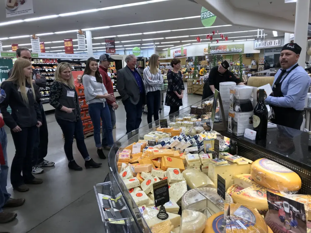 Deal participants stand at a cheese counter.