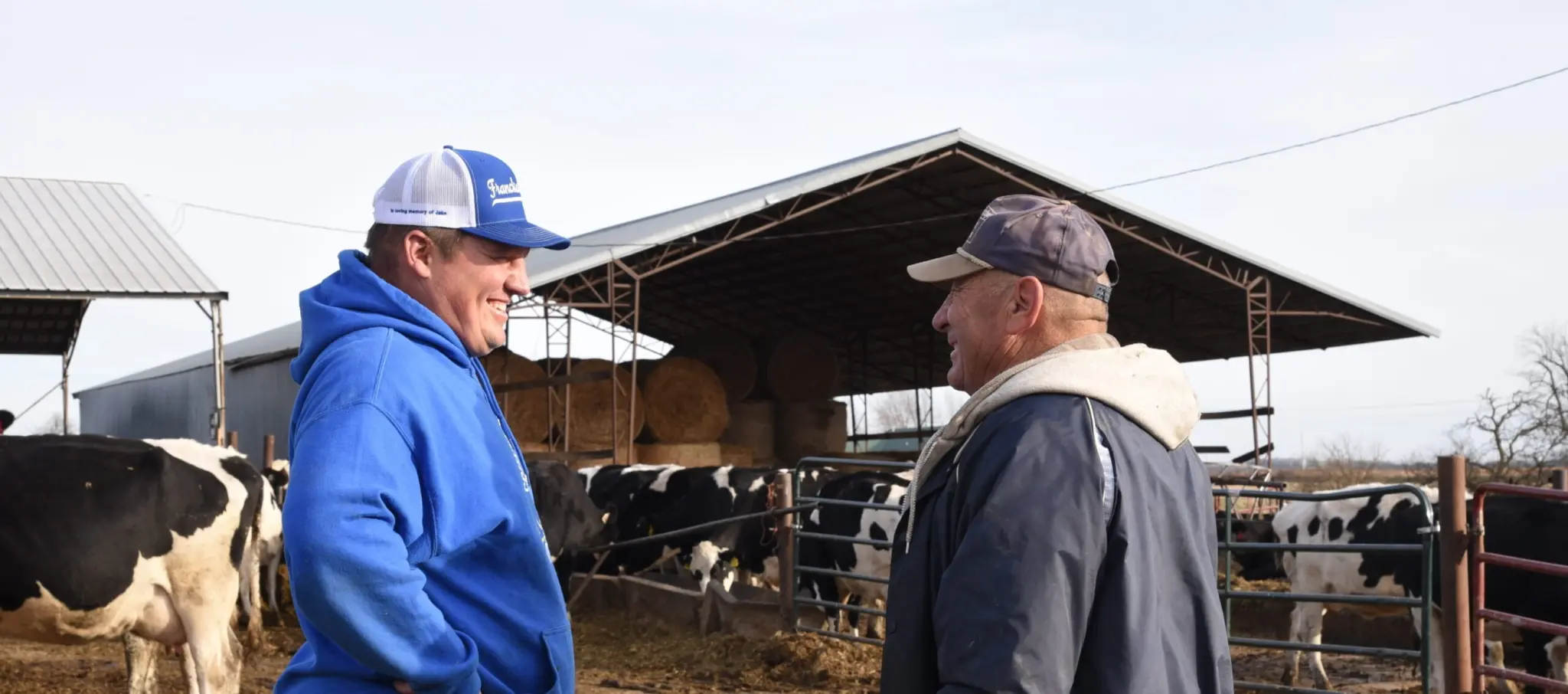 Two farmers talk in front of a cow pen.