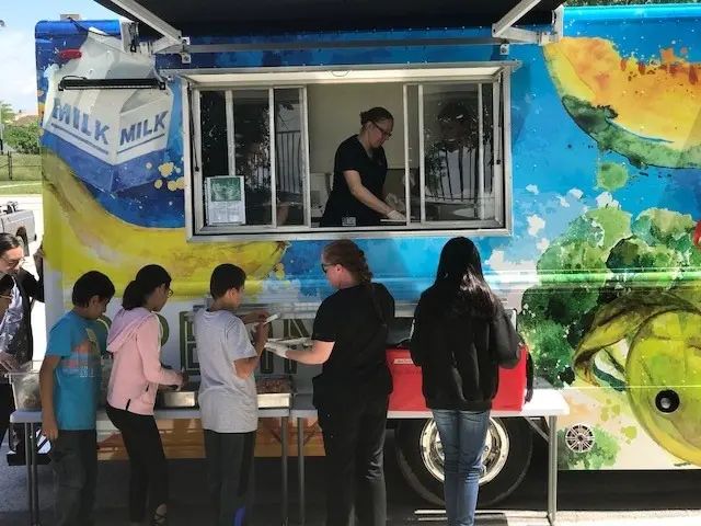 Teens gathered at a food truck, ordering and eating food.