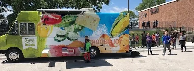 Food truck parked in a parking lot with people gathered around it.
