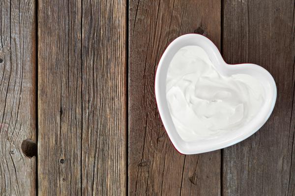 A heart-shaped bowl of yogurt on a wooden board.
