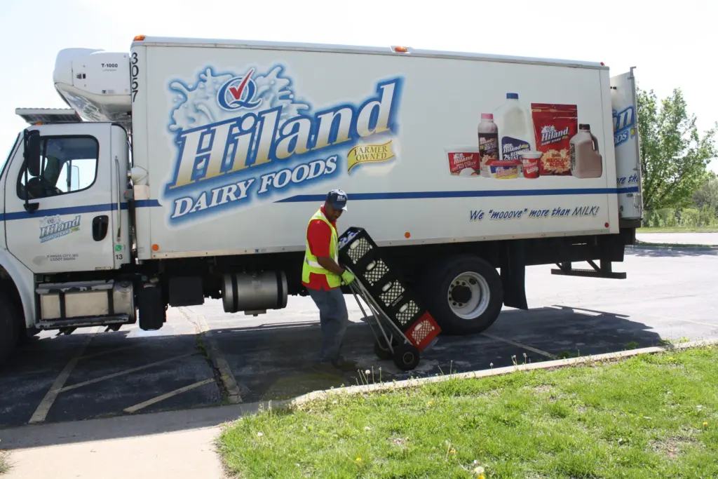 A worker pulls a dolly loaded with crates of milk near his delivery truck.