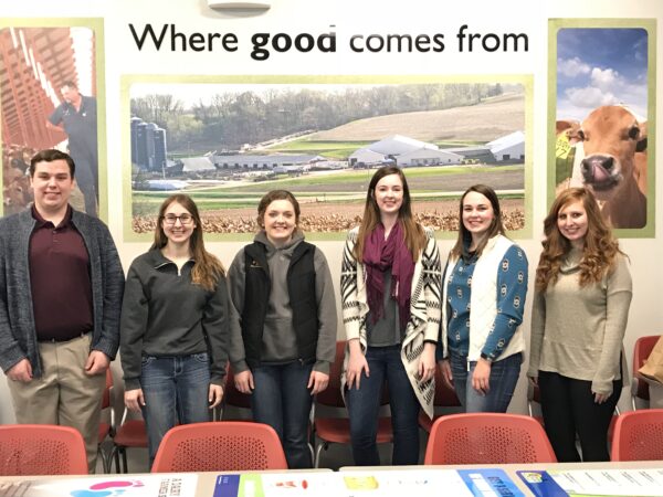 Teens stand in front of a dairy display at a conference.
