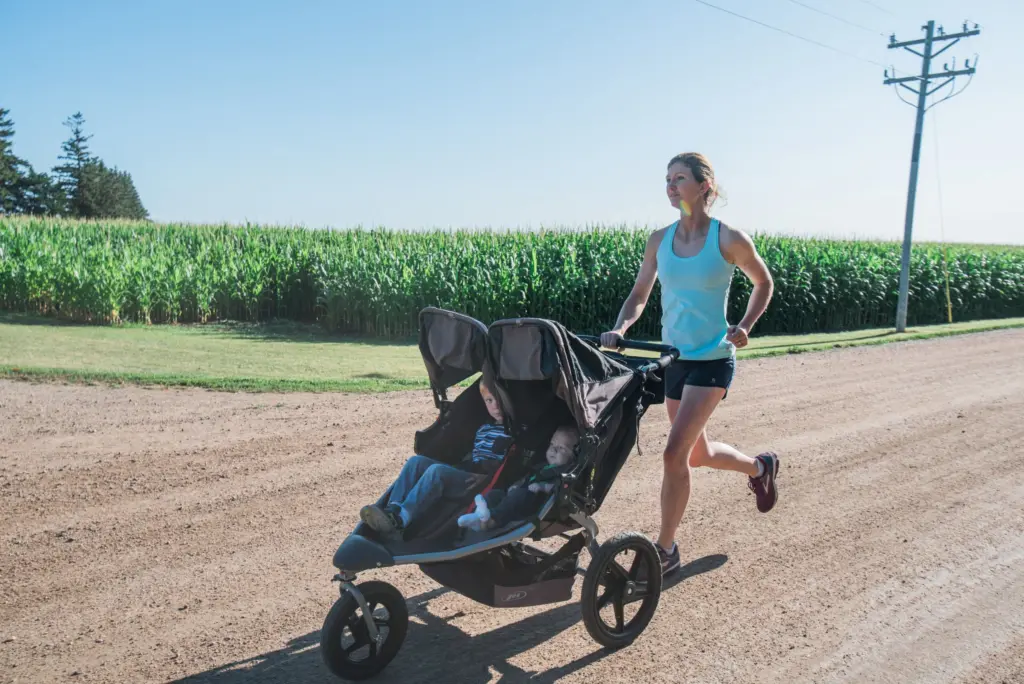 Mom running while pushing a stroller with two boys.