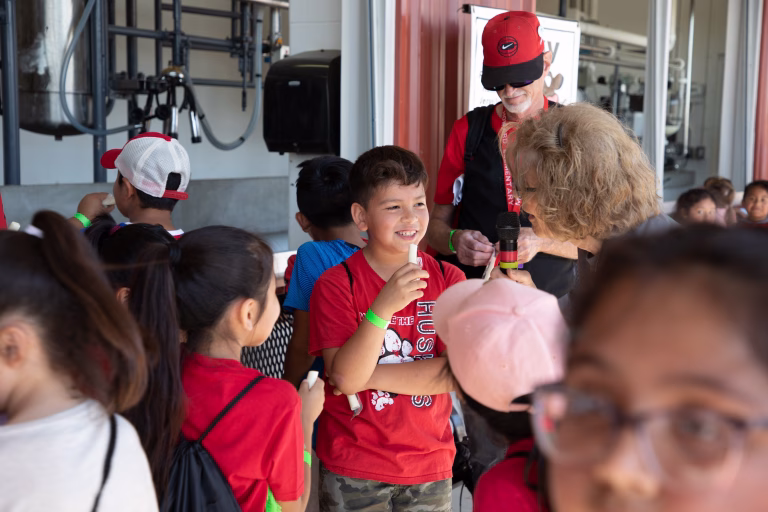 Boy eating a cheese stick and talking to a woman with a microphone