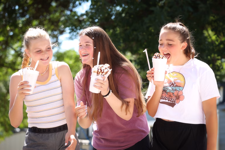 Three young girls laughing and enjoying large cups of ice cream