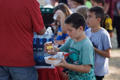 Little boy in teal shirt holding a lunch tray with a carton of chocolate milk