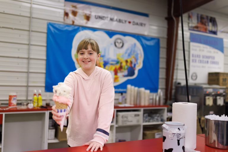 Girl in pink hoodie holding out two scoop ice cream cone