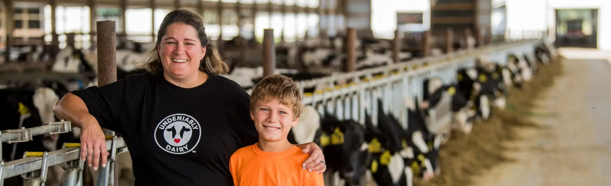Dairy farmer and her son in a barn, with cows in the background.