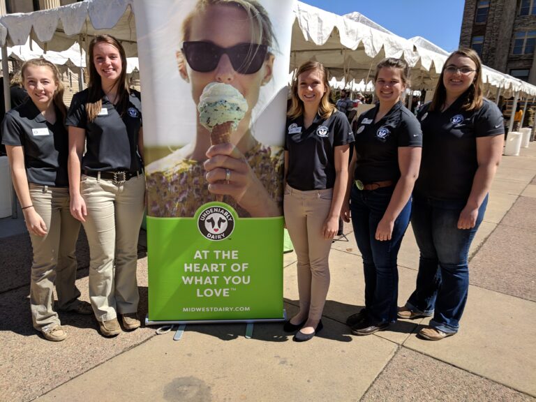 Teen girls stand around an Undeniably Dairy banner at Ag Awareness Day.