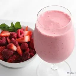 Raspberry strawberry yogurt smoothie next to a bowl of berries.