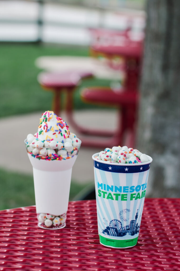 Two birthday cake parfaits sit on a red picnic table.