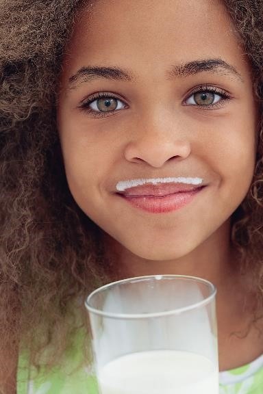 Closeup photo of a girl with a glass of milk and a milk moustache.