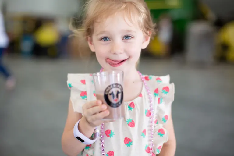 Small girl with her tongue out holds a glass of chocolate milk.