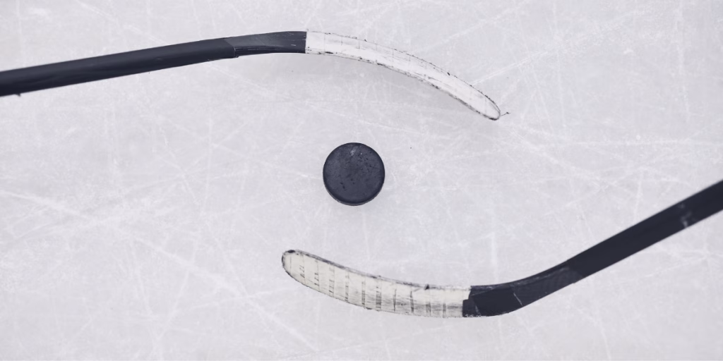 Two hockey sticks circle a puck on the ice