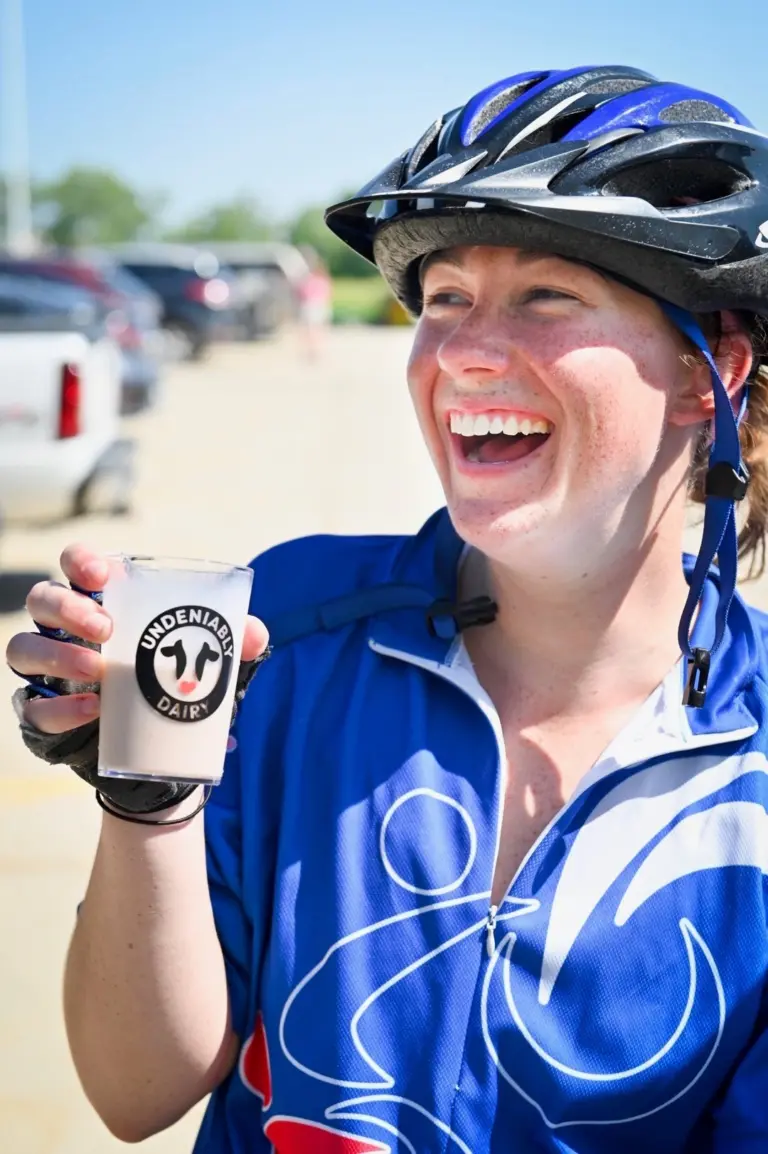 A female in cycling gear holds milk in an Undeniably Dairy glass.